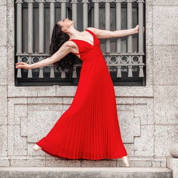 Dancer in long red dress en pointe (ballet shoes), looking up at the sky.