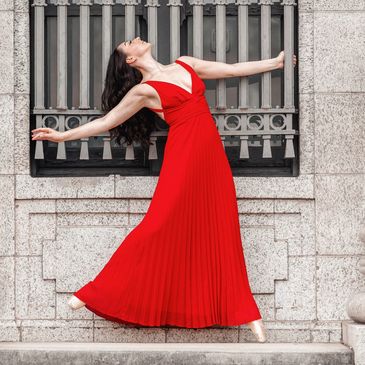 Dancer in long red dress en pointe (ballet shoes), looking up at the sky.