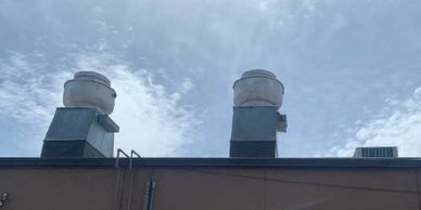 Two industrial vents on a rooftop against a partly cloudy sky.