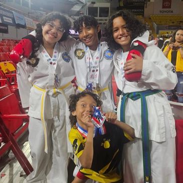 Four young martial artists smiling with medals at a competition.