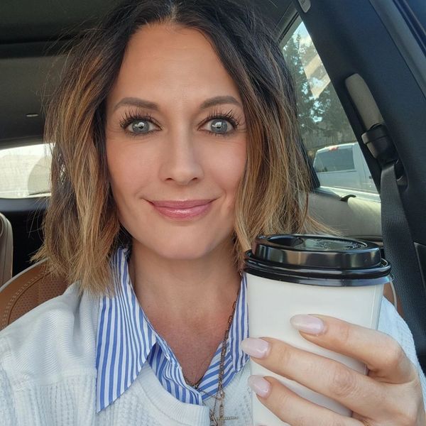 Woman smiling in a car holding a coffee cup.