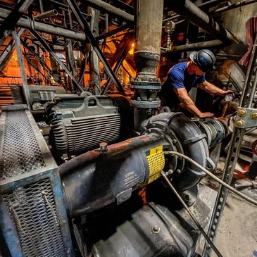 A worker inspects machinery in an industrial setting with warm lighting.