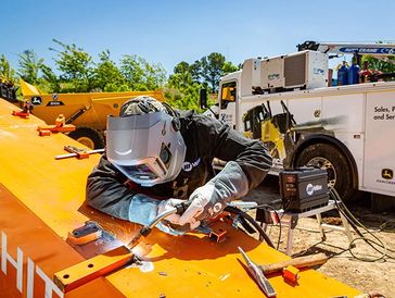 Worker welding metal on bright orange structure outdoors.