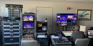 A man operates a video control room with multiple monitors and equipment racks.