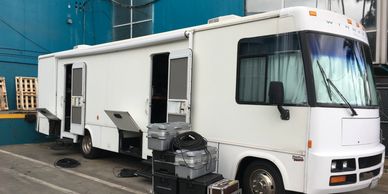 White mobile production or broadcast vehicle with equipment cases outside.