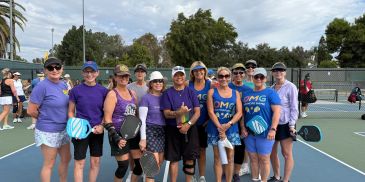 Group of pickleball players posing on a court, some in matching purple shirts.