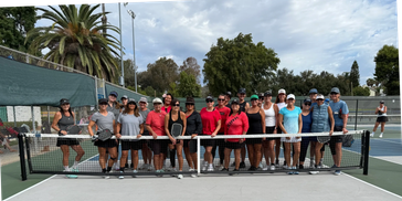 Group of women standing on a tennis court behind the net.