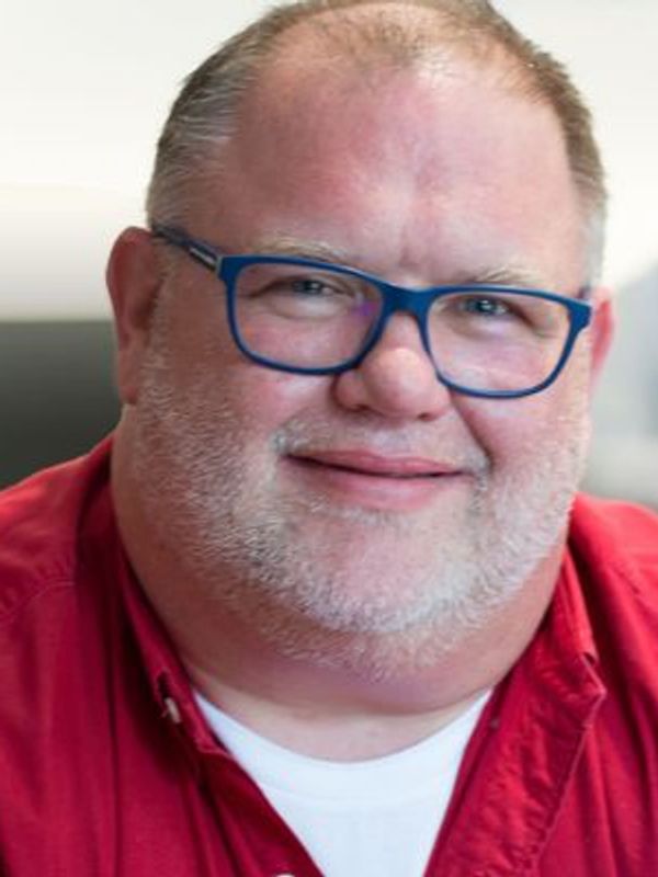 Headshot of a white male with glasses in a red shirt smiling