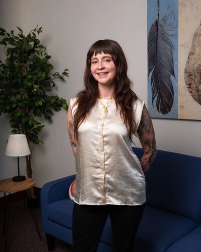 Smiling woman with tattoos stands in a cozy room with art and plants.