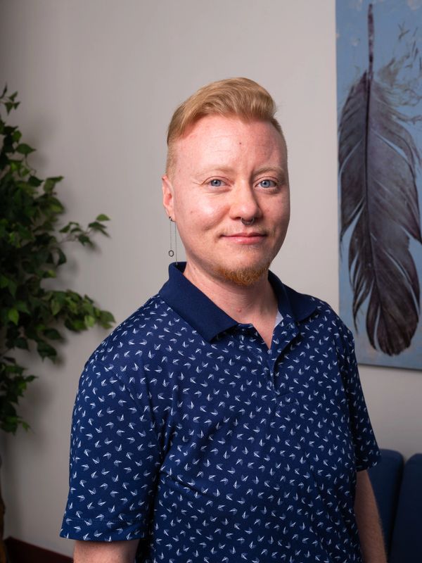 Person with light hair and blue eyes wearing a navy patterned polo shirt.