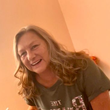 A woman with wavy hair smiling indoors against a peach-colored wall.