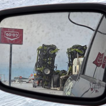 Snowy roadside view reflected in a vehicle's side mirror with farm equipment and a Co-op sign.