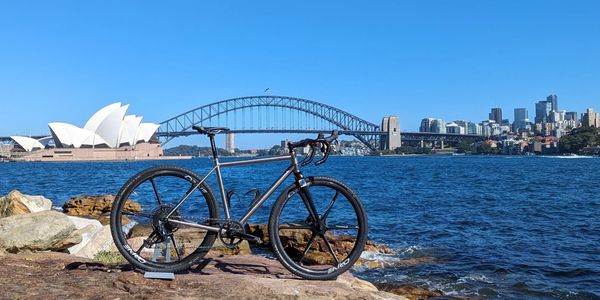 A sleek bicycle parked by Sydney Harbour with Opera House and Harbour Bridge in the background.