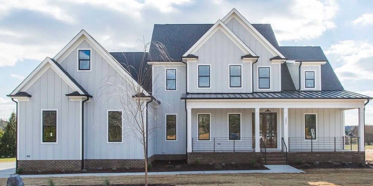 Modern farmhouse with white siding and black roof under a cloudy sky.