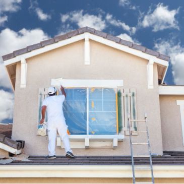 Painter working on house exterior under blue sky.