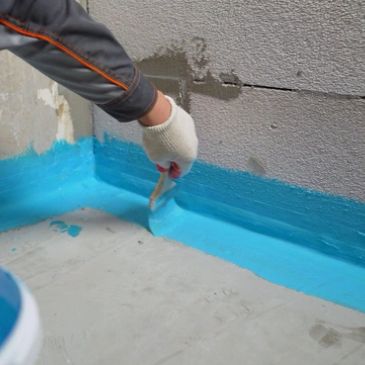 Applying blue waterproof sealant at floor-wall joint.