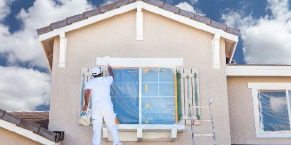 Painter applying white paint on a house exterior.