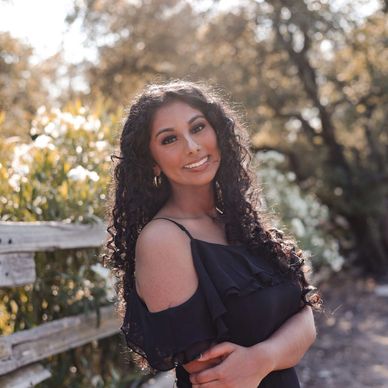 Woman with curly hair smiling outdoors on a sunny day.