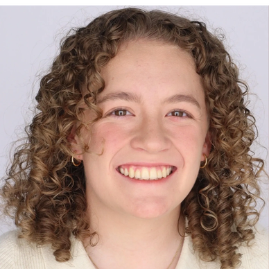 Smiling woman with curly hair and hoop earrings.