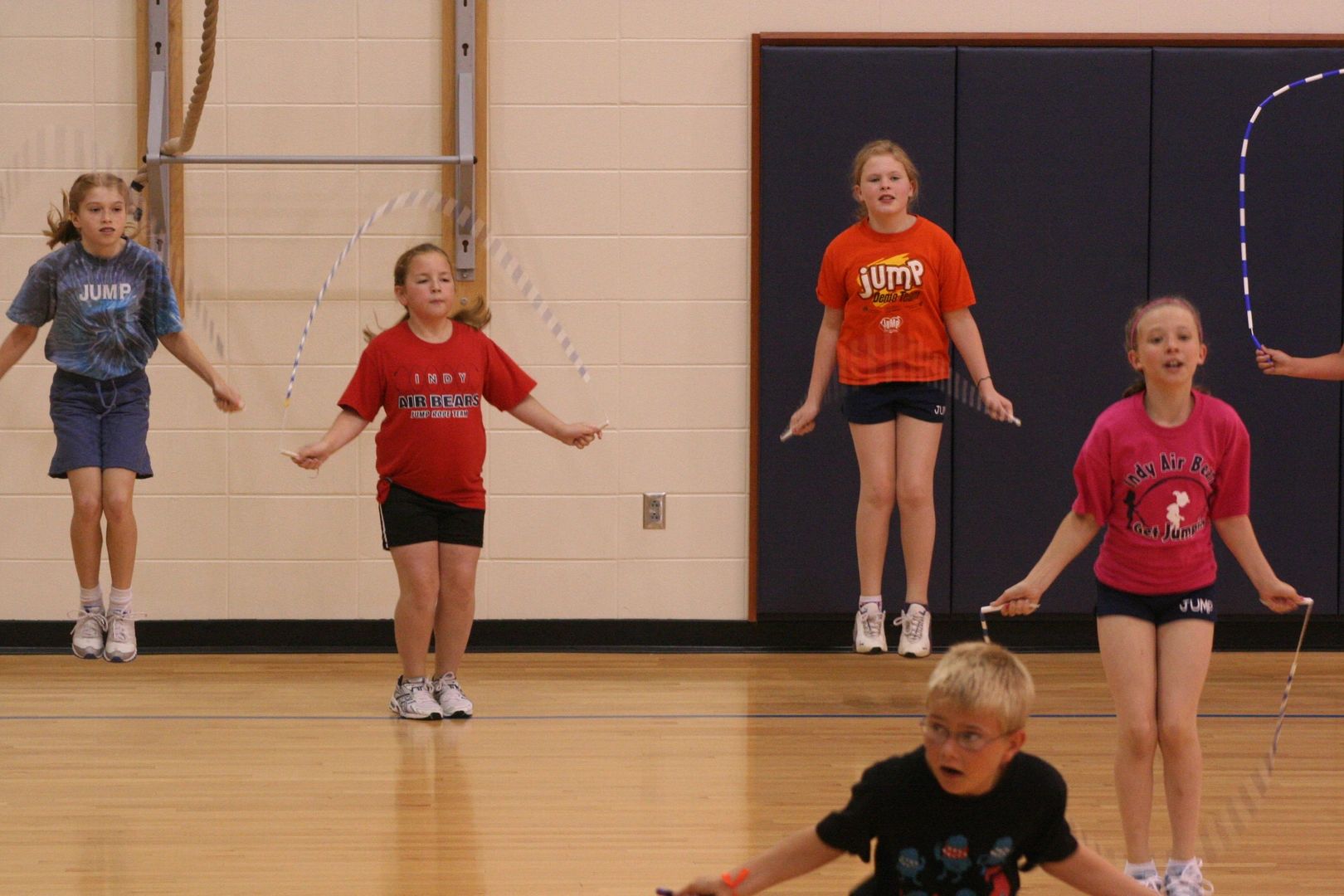 Children jumping rope together in a gymnasium.