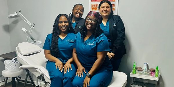 A group of students smiling in the aesthetics lab at beauty school.