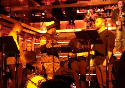 Band performs on stage with vibrant orange lighting.