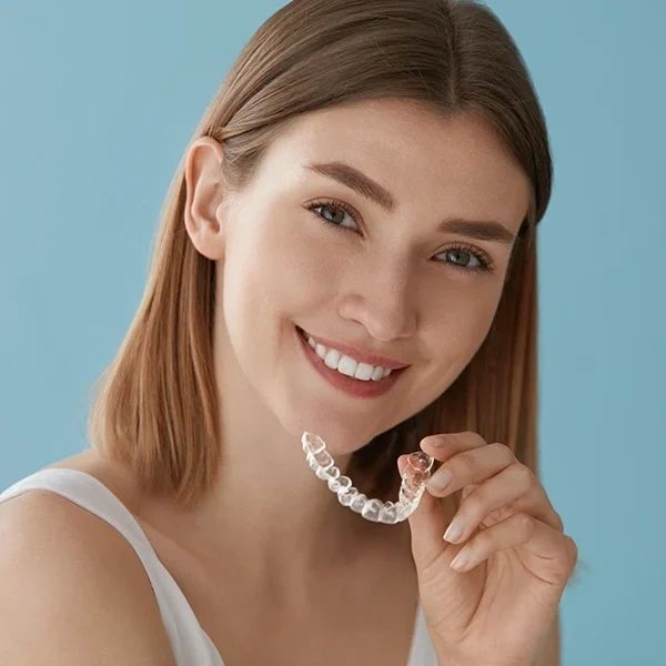Smiling woman holding a clear dental aligner against a blue background.