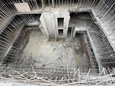 Concrete foundation pit with exposed rebar and elevator shafts under construction.