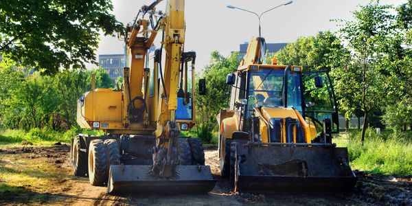 Two yellow construction vehicles parked on a dirt path surrounded by greenery.