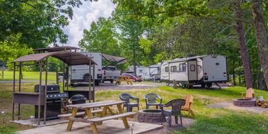 RV sites with picnic tables and fire pits beneath trees at a quiet vacation rental and RV park.