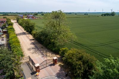 A rural road alongside a green field and gate entrance.