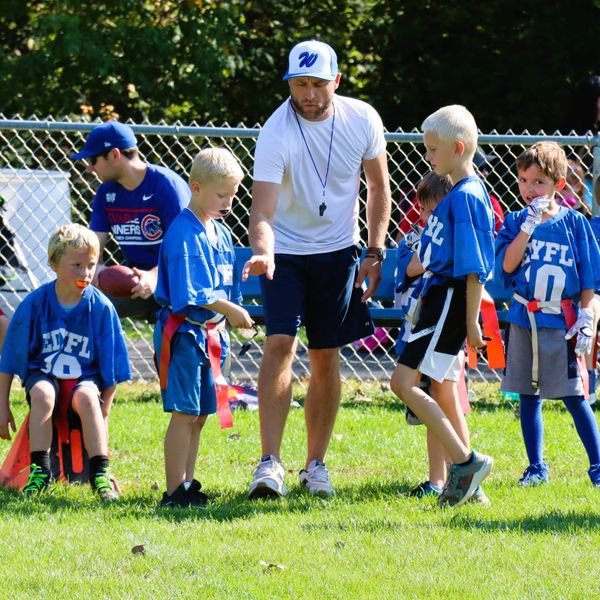 Coach instructing young kids in blue jerseys during a flag football game.