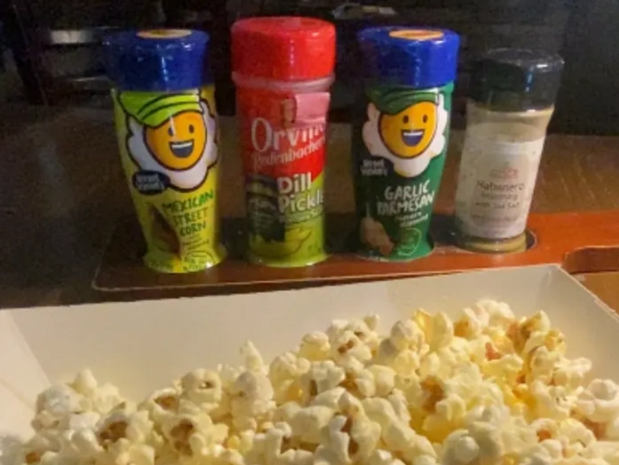 Popcorn with four different seasoning bottles lined up behind it.