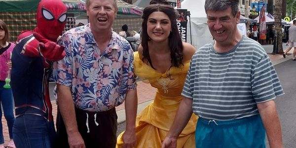 People posing with Spider-Man and a woman in a yellow princess dress at an outdoor event.