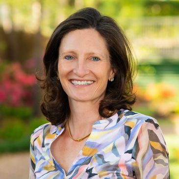 Smiling woman in colorful blouse outdoors with blurred background.