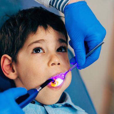 A dentist applies fluoride treatment with a purple light to a young boy.
