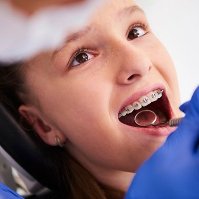 A dentist examines a girl with braces during orthodontic screening for kids.