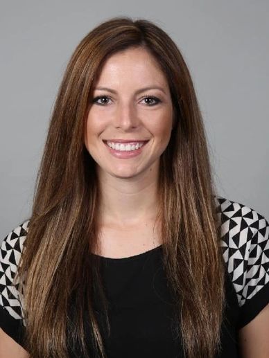 Smiling woman with long brown hair against a gray background.