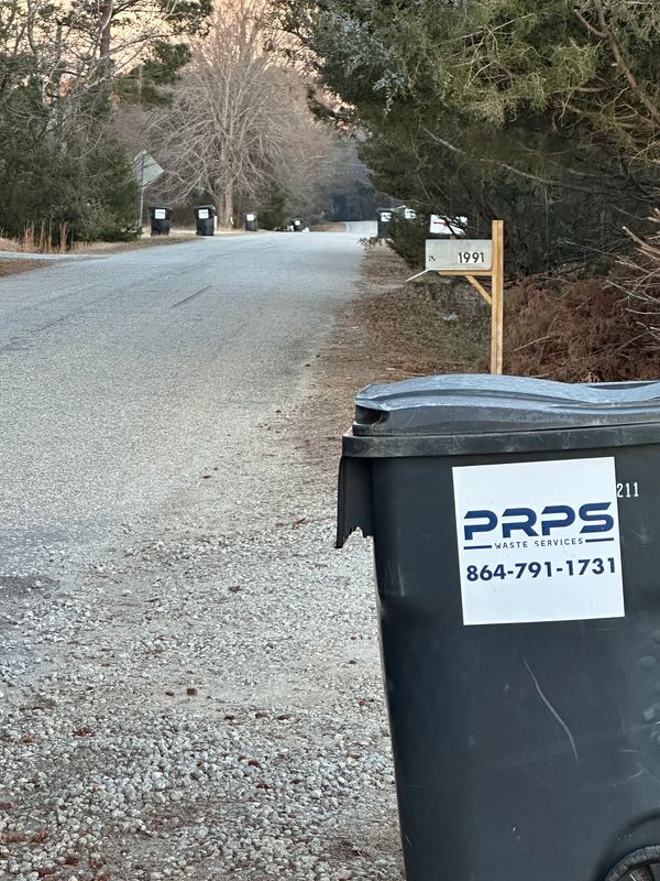 Trash bin with waste service label on a rural roadside.