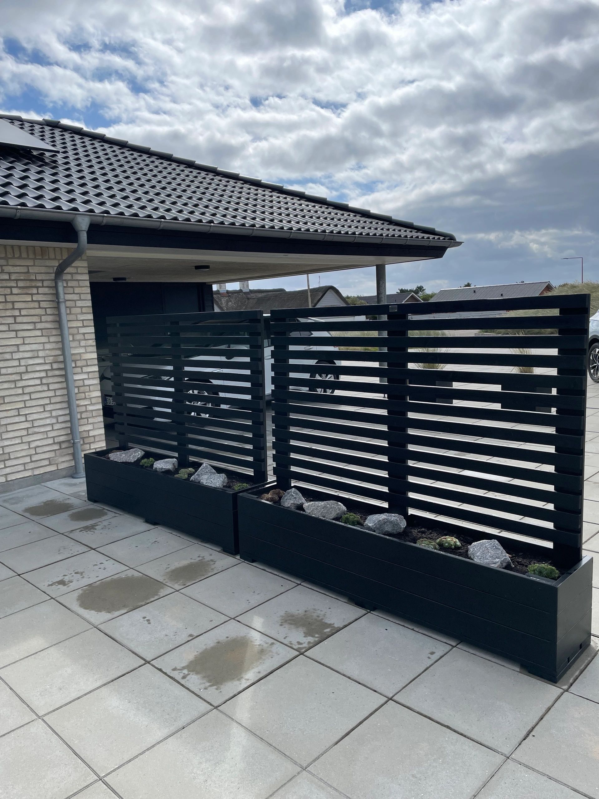 Modern house exterior with black slatted fence and cloudy sky.