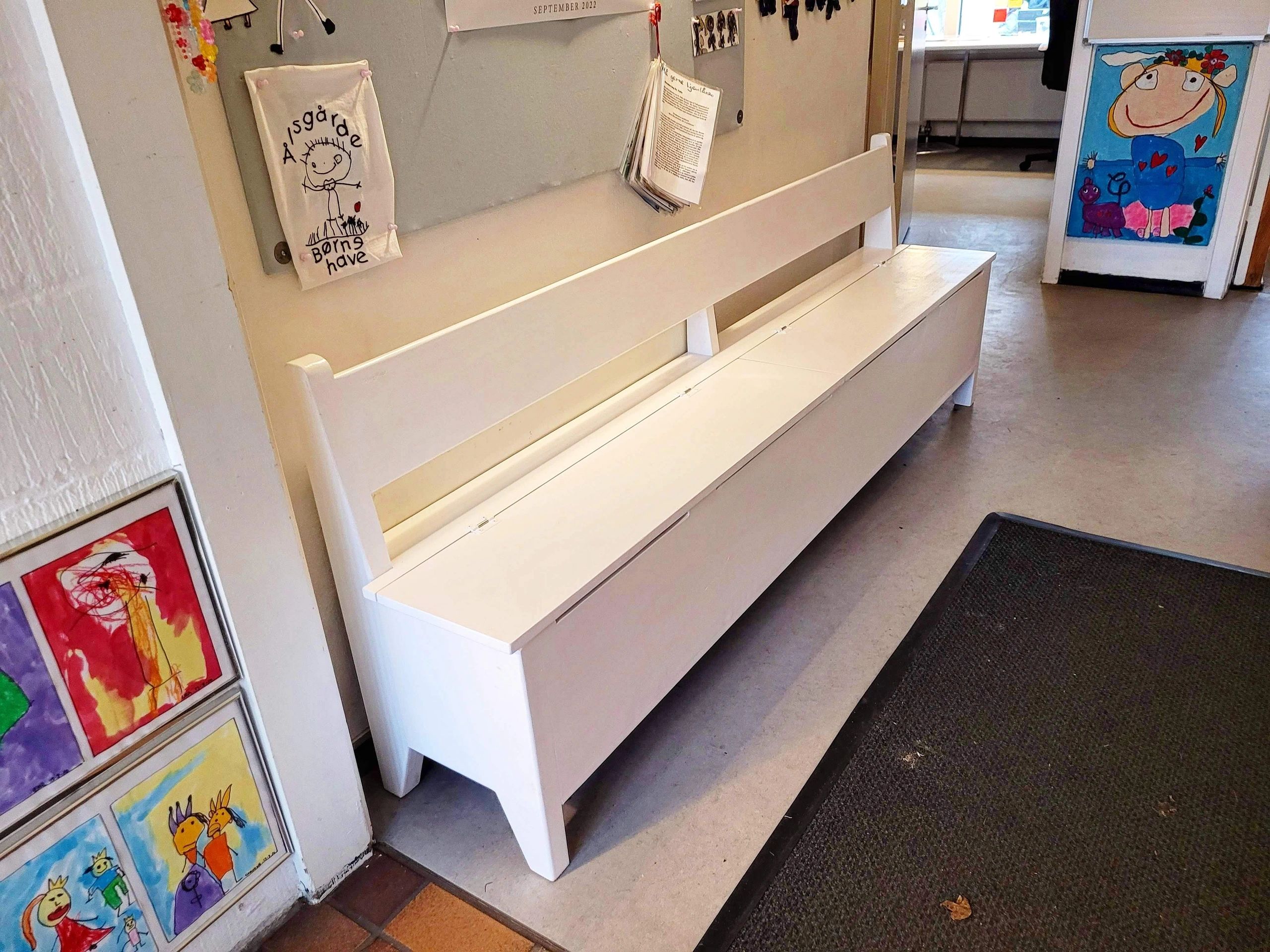 White bench in a colorful, child-friendly hallway with drawings on walls.