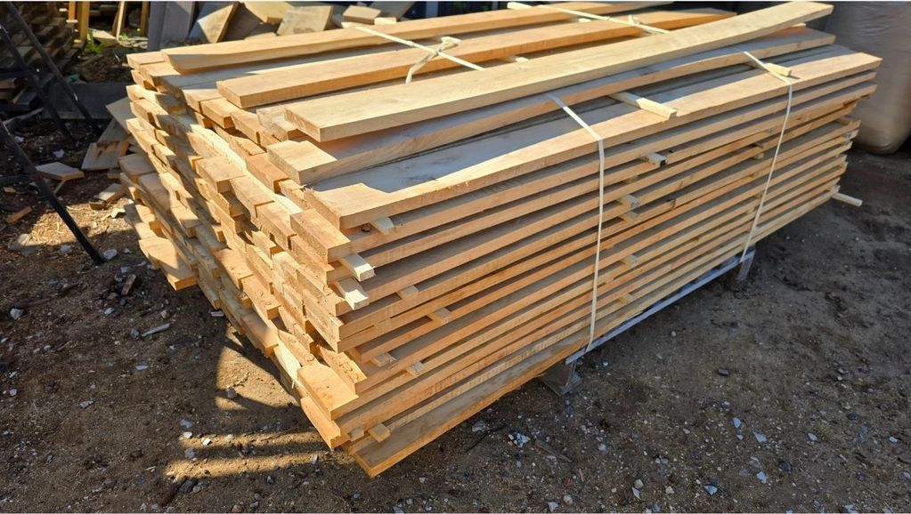 Stack of neatly arranged wooden planks tied together outdoors.