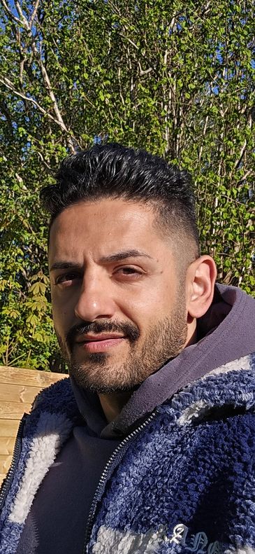 Man with short black hair and beard wearing a blue fleece jacket outdoors.