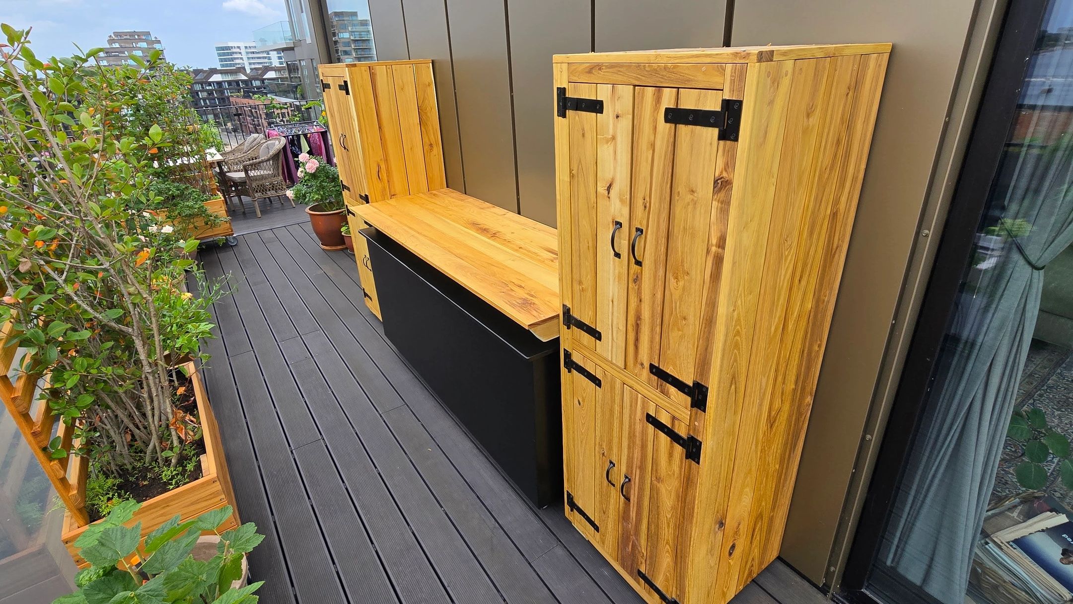 Wooden cabinets and plants on a balcony with city view.