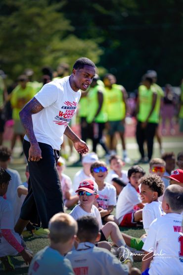 Coach engaging with kids at an outdoor sports event on a sunny day.