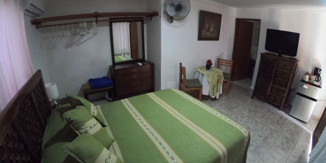 Cozy bedroom with green bedspread, wooden furniture, and a small dining area.