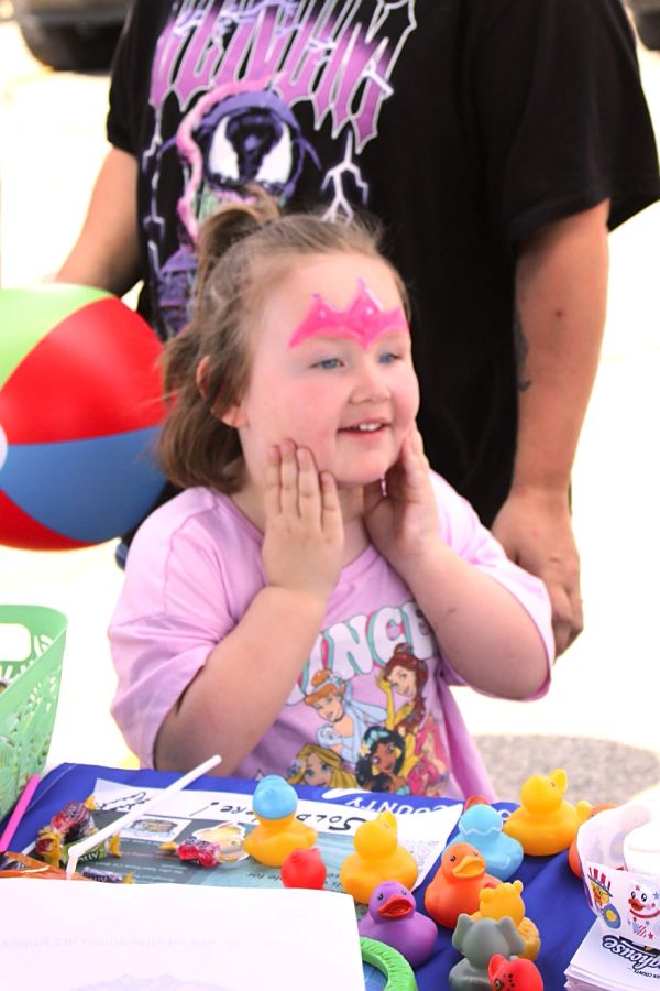 Smiling girl with face paint playing with colorful rubber ducks.