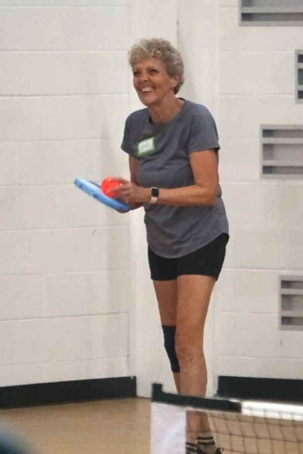 Woman smiling and holding a paddle with ball indoors.