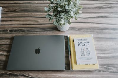 A closed MacBook, two books, and a plant on a wooden table.