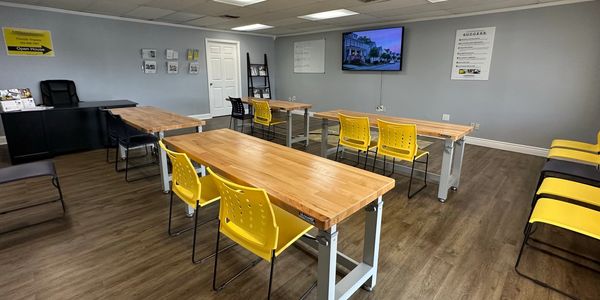 Modern classroom with wooden desks and yellow chairs arranged neatly for real estate certification. 